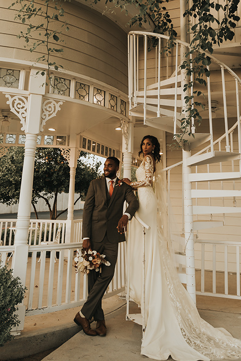  A dreamy amber toned wedding in Arizona at a wedgewood wedding venue – with the bride in a long sleeve lace gown and the bridesmaids in burnt orange dresses and the groom in a café brown suit and the groomsmen in a tan suit – couple standing on the stairs
