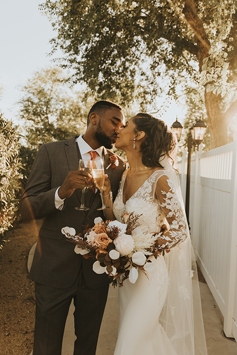  A dreamy amber toned wedding in Arizona at a wedgewood wedding venue – with the bride in a long sleeve lace gown and the bridesmaids in burnt orange dresses and the groom in a café brown suit and the groomsmen in a tan suit – couple cheersing