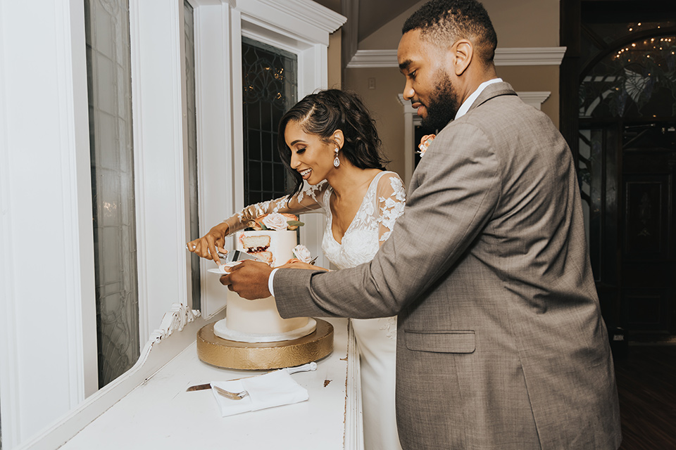 A dreamy amber toned wedding in Arizona at a wedgewood wedding venue – with the bride in a long sleeve lace gown and the bridesmaids in burnt orange dresses and the groom in a café brown suit and the groomsmen in a tan suit – couple cutting the cake together