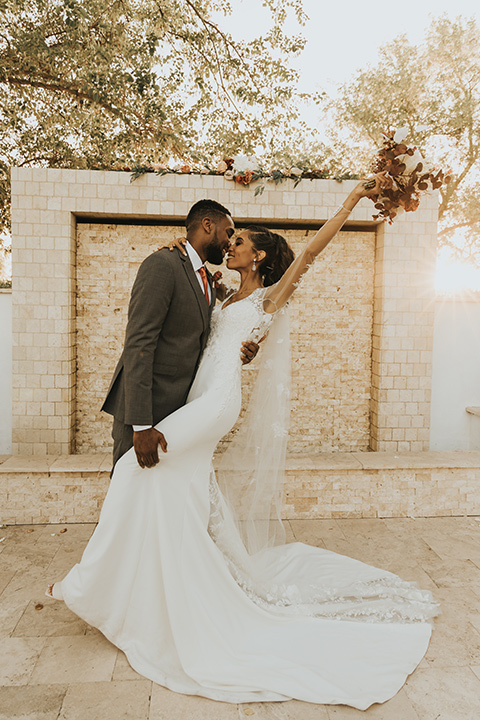  A dreamy amber toned wedding in Arizona at a wedgewood wedding venue – with the bride in a long sleeve lace gown and the bridesmaids in burnt orange dresses and the groom in a café brown suit and the groomsmen in a tan suit – first kiss