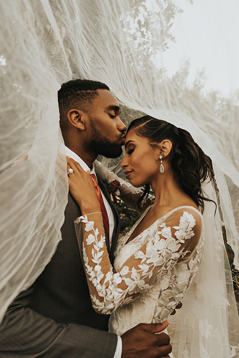  A dreamy amber toned wedding in Arizona at a wedgewood wedding venue – with the bride in a long sleeve lace gown and the bridesmaids in burnt orange dresses and the groom in a café brown suit and the groomsmen in a tan suit – couple standing on the stairs