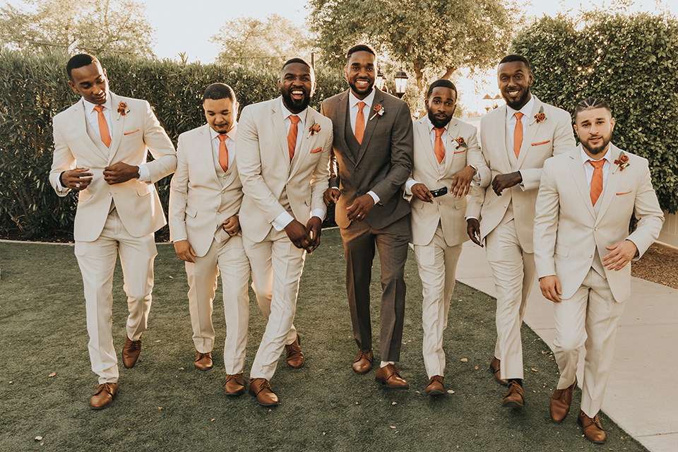 A dreamy amber toned wedding in Arizona at a wedgewood wedding venue – with the bride in a long sleeve lace gown and the bridesmaids in burnt orange dresses and the groom in a café brown suit and the groomsmen in a tan suit – groomsmen walking together