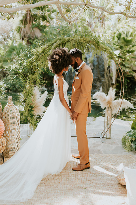  bohemian wedding with the bride in a flowing lace gown and the groom in a caramel brown suit with a green velvet bow tie- couple heads touching