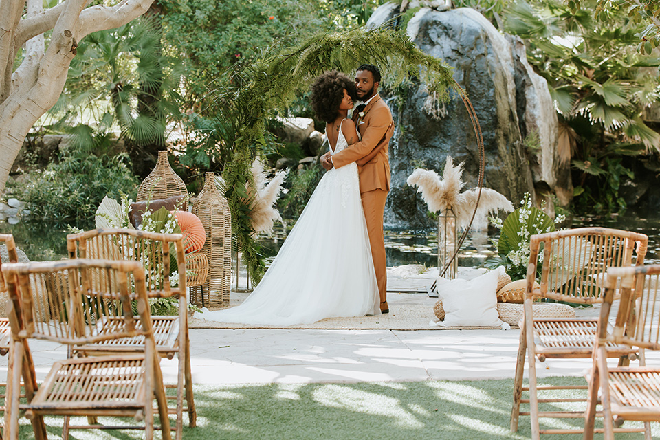  bohemian wedding with the bride in a flowing lace gown and the groom in a caramel brown suit with a green velvet bow tie- couple kissing at the ceremony