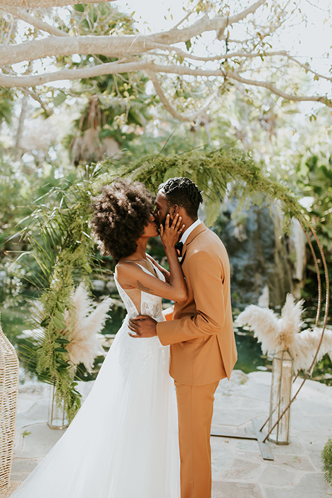  bohemian wedding with the bride in a flowing lace gown and the groom in a caramel brown suit with a green velvet bow tie- couple kissing 