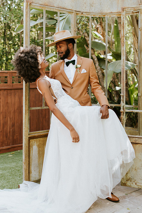  bohemian wedding with the bride in a flowing lace gown and the groom in a caramel brown suit with a green velvet bow tie- groom dipping he bride 