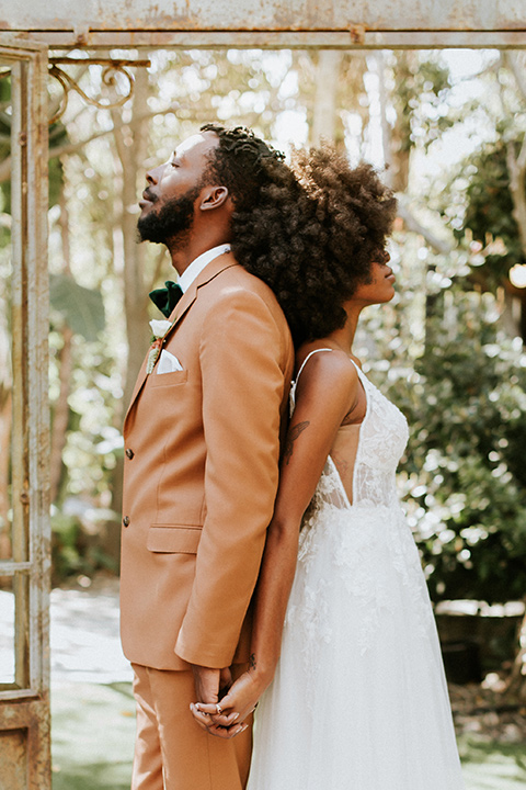  bohemian wedding with the bride in a flowing lace gown and the groom in a caramel brown suit with a green velvet bow tie- couple back to back