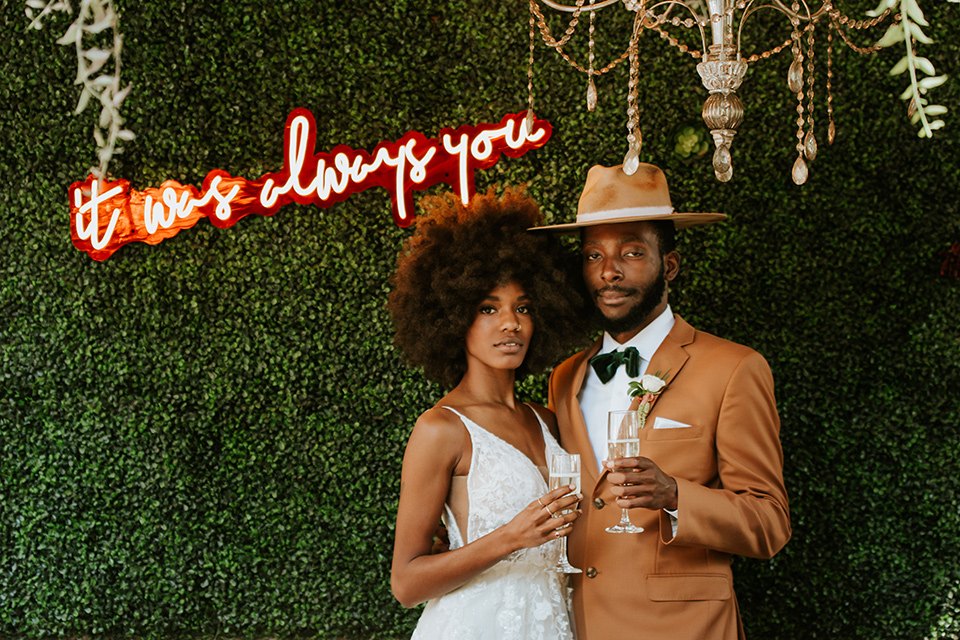  bohemian wedding with the bride in a flowing lace gown and the groom in a caramel brown suit with a green velvet bow tie- couple by the neon sign