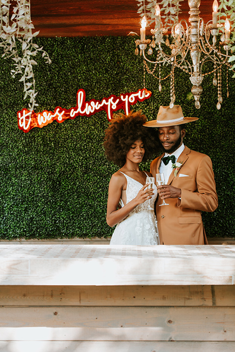 bohemian wedding with the bride in a flowing lace gown and the groom in a caramel brown suit with a green velvet bow tie- couple with the neon sign