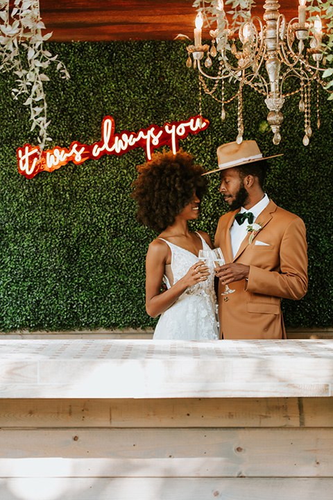  bohemian wedding with the bride in a flowing lace gown and the groom in a caramel brown suit with a green velvet bow tie- couple with our neon sign 