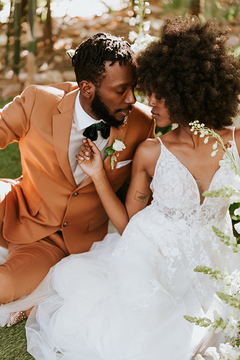  bohemian wedding with the bride in a flowing lace gown and the groom in a caramel brown suit with a green velvet bow tie- couple sitting on the ground