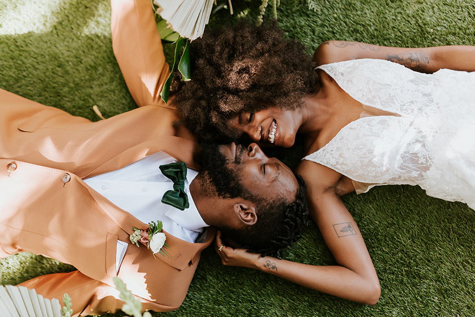  bohemian wedding with the bride in a flowing lace gown and the groom in a caramel brown suit with a green velvet bow tie- couple laying in the grass