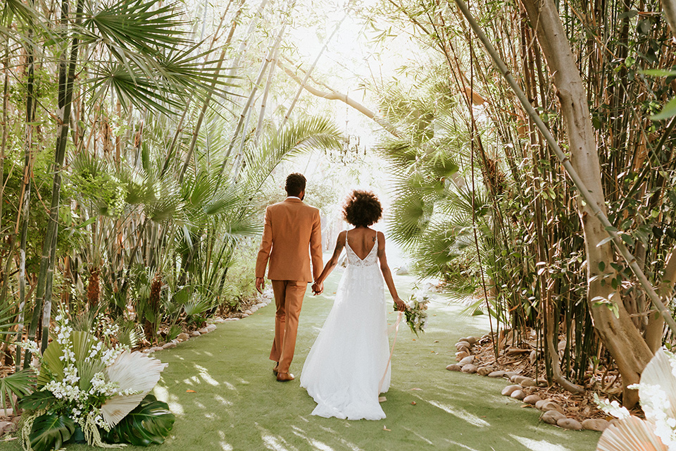  bohemian wedding with the bride in a flowing lace gown and the groom in a caramel brown suit with a green velvet bow tie- couple walking in the venue