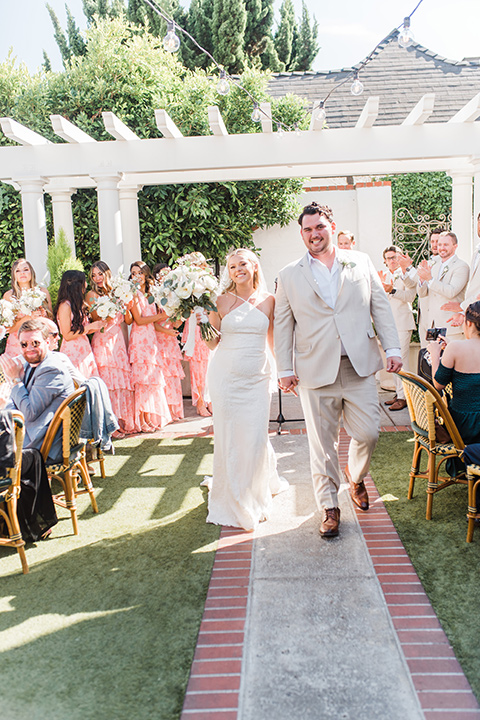  tan and pink garden wedding with floral bridesmaid dresses and the groom and groomsmen in tan suits – walking down the aisle 