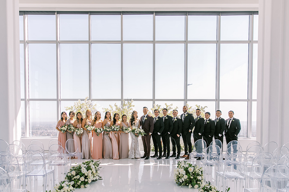 A city wedding with the guys in burgundy and black tuxedos and the bridesmaids in blush dresses- bridal party in a line