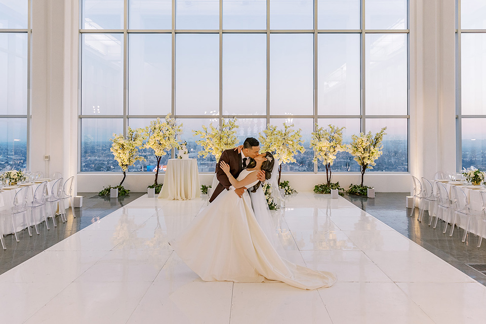 A city wedding with the guys in burgundy and black tuxedos and the bridesmaids in blush dresses- couple kissing on the dancefloor at the reception