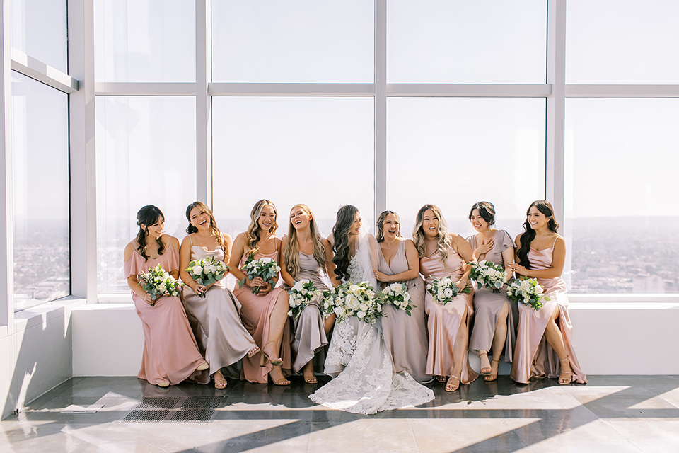A city wedding with the guys in burgundy and black tuxedos and the bridesmaids in blush dresses- bridesmaids and the bride looking at each other