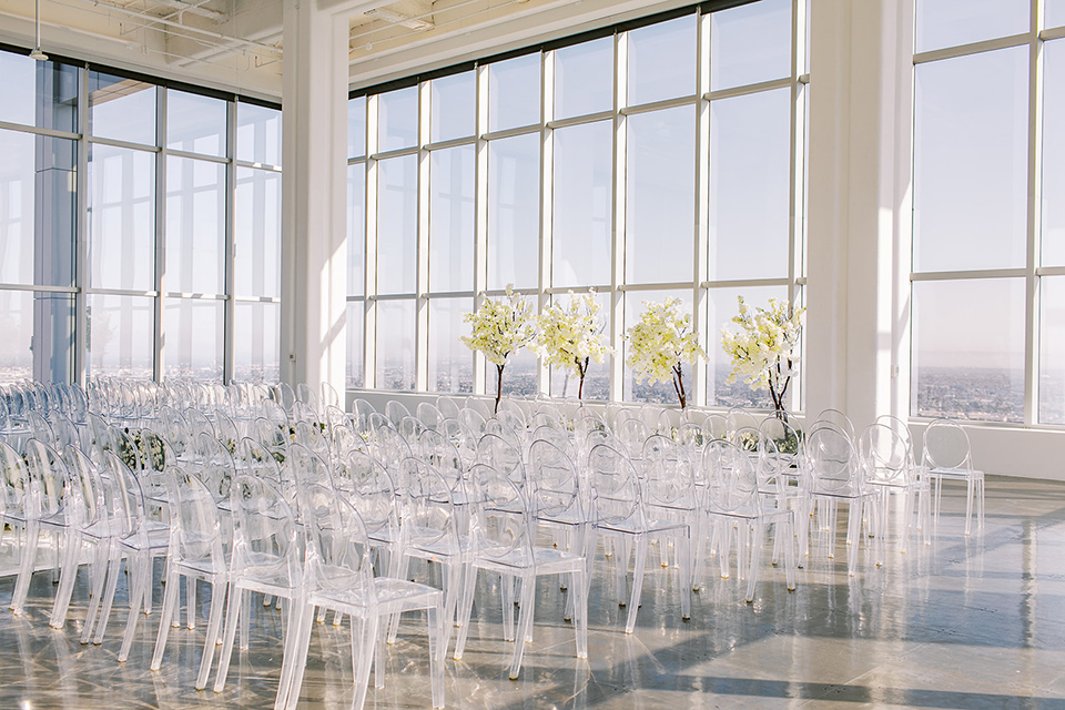 A city wedding with the guys in burgundy and black tuxedos and the bridesmaids in blush dresses- ceremony space with clear modern chairs and big wall to wall windows