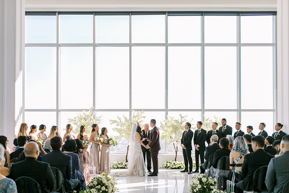 A city wedding with the guys in burgundy and black tuxedos and the bridesmaids in blush dresses- ceremony space with the bride and groom kissing