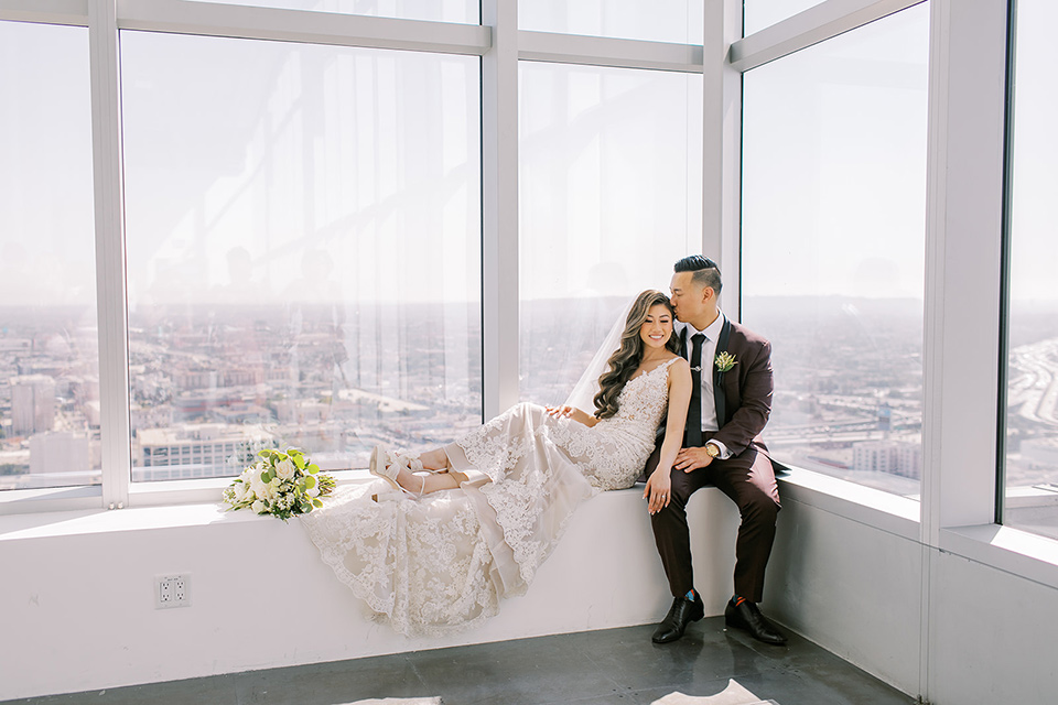 A city wedding with the guys in burgundy and black tuxedos and the bridesmaids in blush dresses- couple sitting on the windows