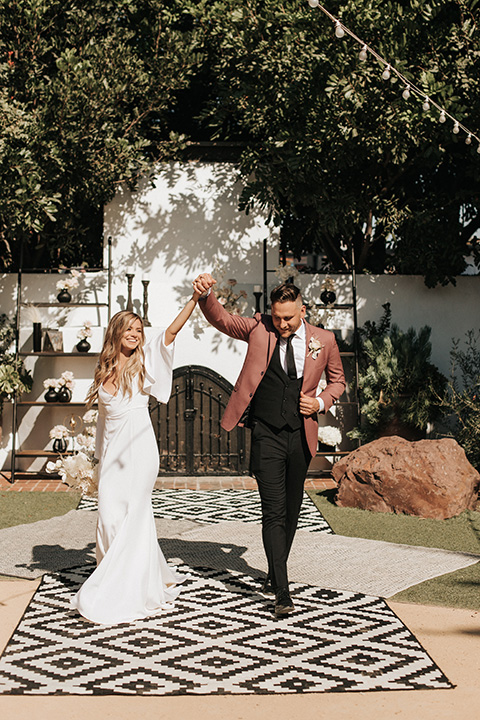  boho wedding with the bride in a modern lace gown with flutter sleeves and the groom in a rose coat with black pants 