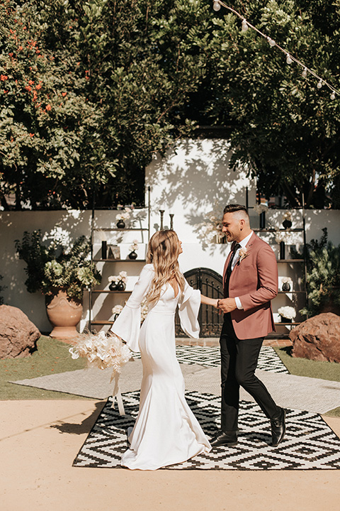  boho wedding with the bride in a modern lace gown with flutter sleeves and the groom in a rose coat with black pants 