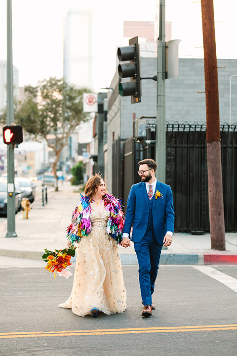  a colorful disco wedding in dtla with the bride in a champagne gown with metallic stars and the groom in a cobalt blue suit – couple walking in the street 