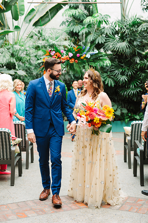  a colorful disco wedding in dtla with the bride in a champagne gown with metallic stars and the groom in a cobalt blue suit – couple walking down the aisle 