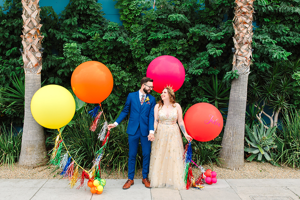  a colorful disco wedding in dtla with the bride in a champagne gown with metallic stars and the groom in a cobalt blue suit – couple kissing with balloons