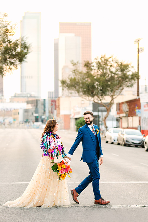  a colorful disco wedding in dtla with the bride in a champagne gown with metallic stars and the groom in a cobalt blue suit – couple walking in the street 