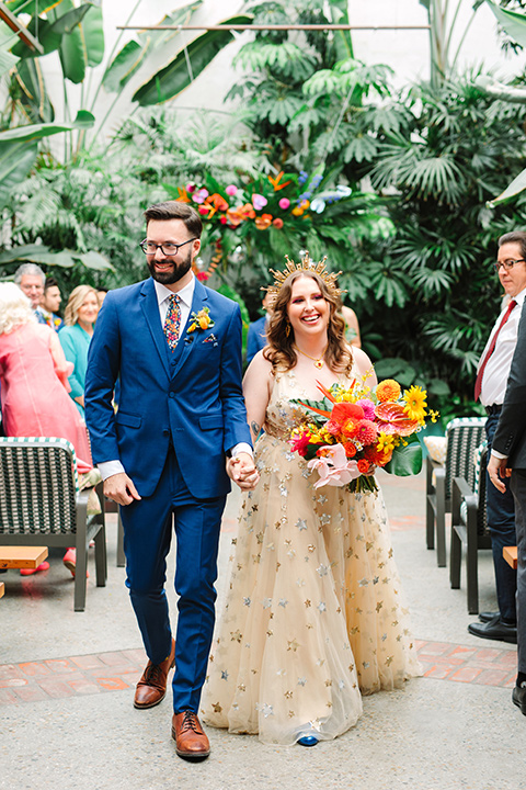  a colorful disco wedding in dtla with the bride in a champagne gown with metallic stars and the groom in a cobalt blue suit – couple walking down the aisle 