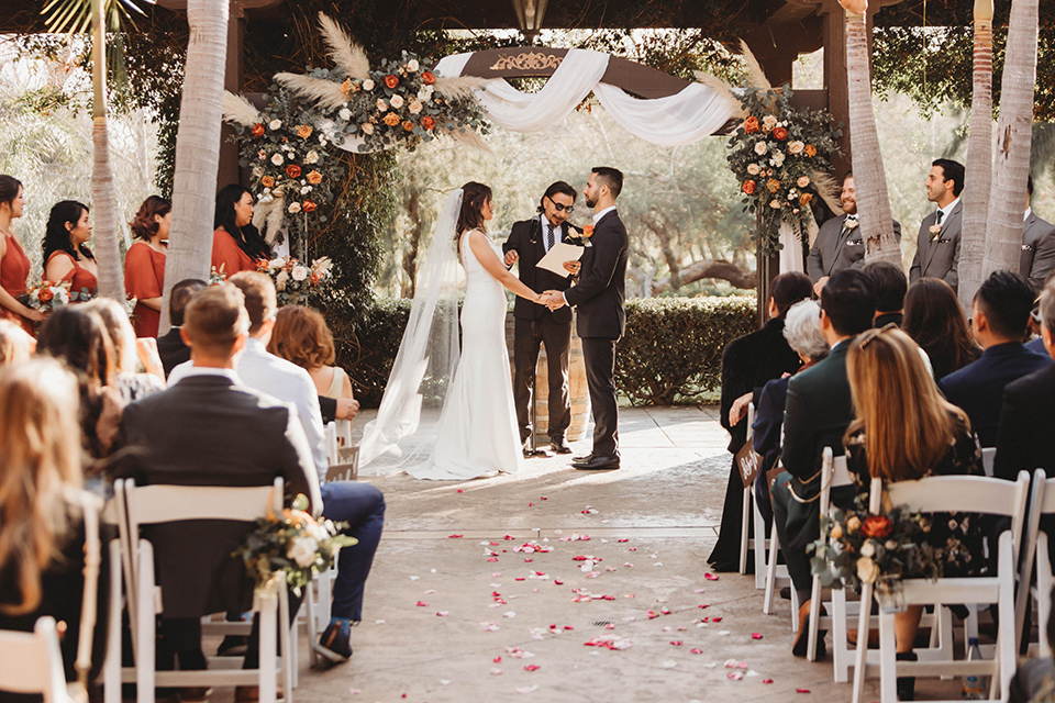  a fall toned wedding at the Fallbrook Estate Wedgewood venue with the groom and groomsmen in grey suits and the bridesmaids in orange – couple at the ceremony 