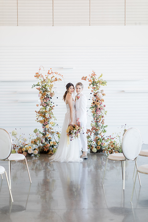 Modern romantic city wedding with an all-white color scheme and bright florals – one bride wore a strapless a-line gown and the other bride wore a white suit – brides saying their vows