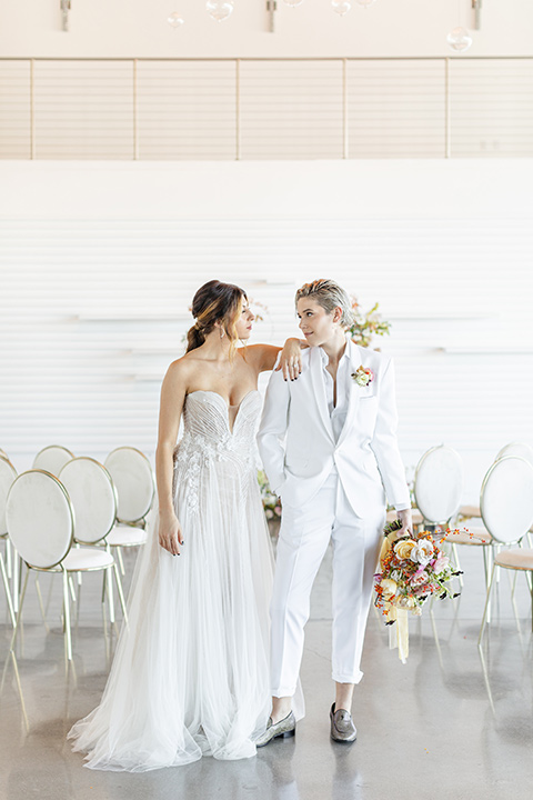 Modern romantic city wedding with an all-white color scheme and bright florals – one bride wore a strapless a-line gown and the other bride wore a white suit – brides cheersing