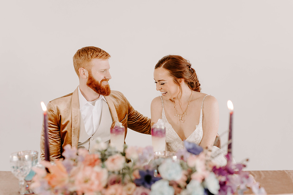  pastel and gold wedding with celestial décor – and the groom in a tan suit and a gold velvet tuxedo – couple sitting at the sweetheart table 