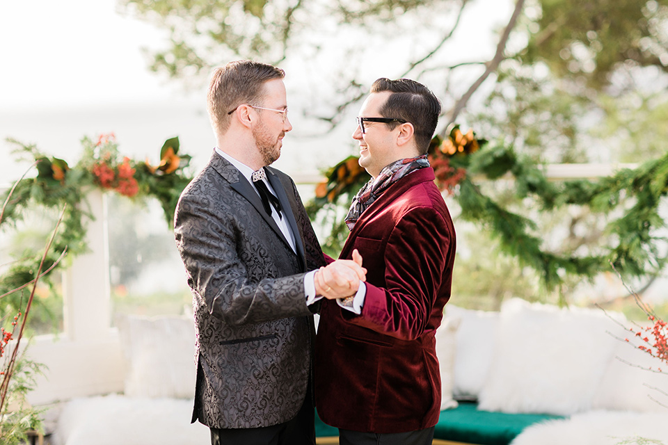  romantic winter inspired wedding theme with luxe textures and details, one groom wore a burgundy velvet shawl tuxedo and the other groom in a black paisley tuxedo – grooms dancing