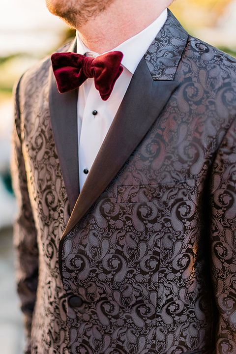  romantic winter inspired wedding theme with luxe textures and details, one groom wore a burgundy velvet shawl tuxedo and the other groom in a black paisley tuxedo – groom in a black paisley tuxedo