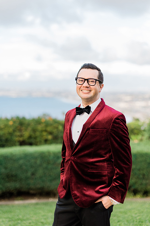  romantic winter inspired wedding theme with luxe textures and details, one groom wore a burgundy velvet shawl tuxedo and the other groom in a black paisley tuxedo – groom in a burgundy velvet tuxedo