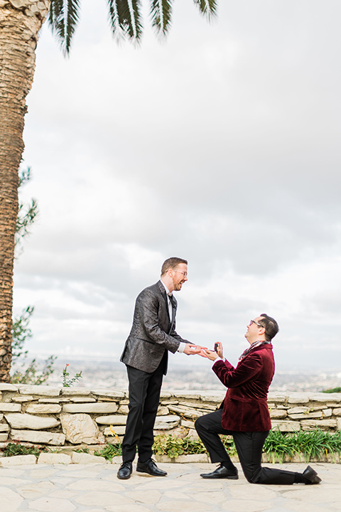  romantic winter inspired wedding theme with luxe textures and details, one groom wore a burgundy velvet shawl tuxedo and the other groom in a black paisley tuxedo – groom models proposing to eachother