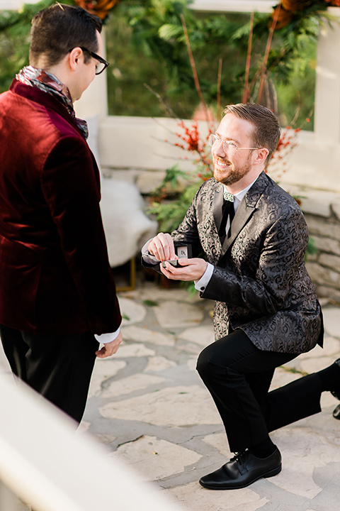  romantic winter inspired wedding theme with luxe textures and details, one groom wore a burgundy velvet shawl tuxedo and the other groom in a black paisley tuxedo – groom models proposing to eachother 
