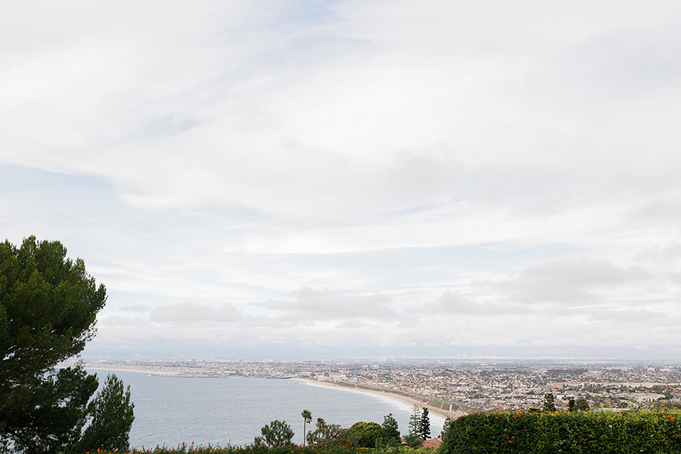  romantic winter inspired wedding theme with luxe textures and details, one groom wore a burgundy velvet shawl tuxedo and the other groom in a black paisley tuxedo – the venue’s view overlooking the pacific ocean