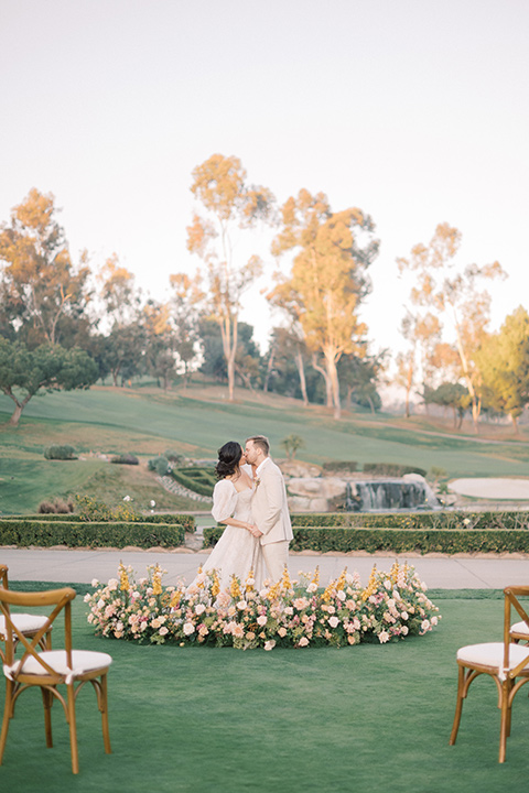  a neutral romantic wedding with touches of peach colors and the groom in a tan suit- couple at the ceremony 
