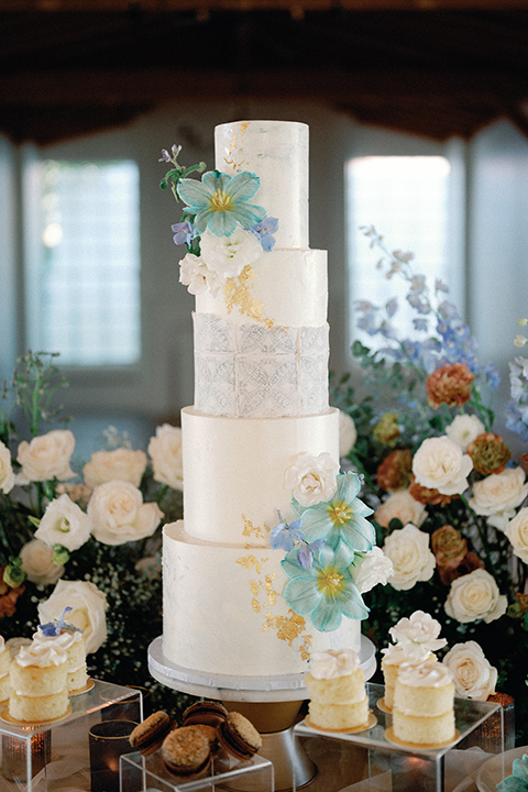 a wedding at the grand gimeno with white, blue, and gold accents – the bride wore a long sleeved modern fitted gown and the groom wore a light blue suit with velvet bow tie – a four tiered cake with blue flowers