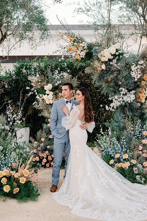 a wedding at the grand gimeno with white, blue, and gold accents – the bride wore a long sleeved modern fitted gown and the groom wore a light blue suit with velvet bow tie – couples at ceremony 