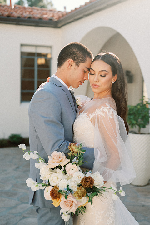 a wedding at the grand gimeno with white, blue, and gold accents – the bride wore a long sleeved modern fitted gown and the groom wore a light blue suit with velvet bow tie – couple outside the venue