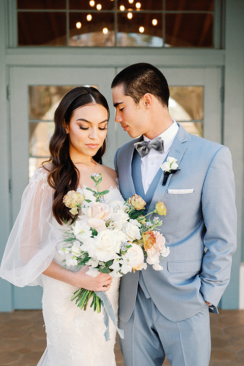 a wedding at the grand gimeno with white, blue, and gold accents – the bride wore a long sleeved modern fitted gown and the groom wore a light blue suit with velvet bow tie – couple outside the venue 