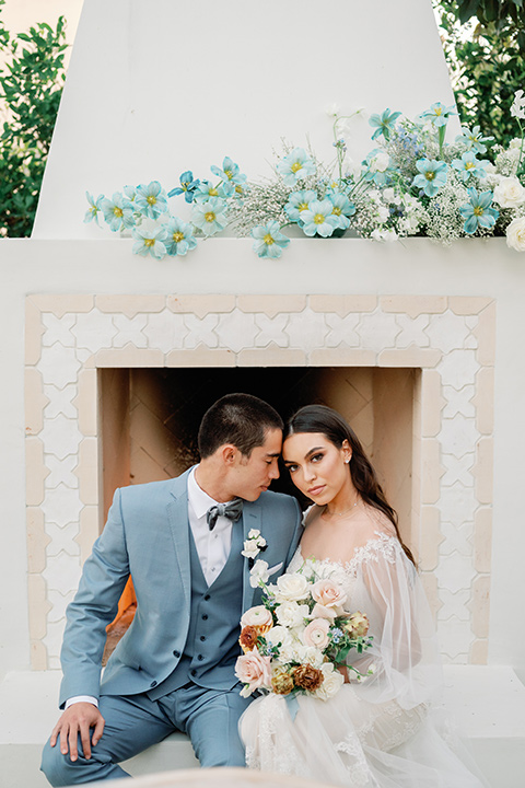 a wedding at the grand gimeno with white, blue, and gold accents – the bride wore a long sleeved modern fitted gown and the groom wore a light blue suit with velvet bow tie – couple sitting outside 