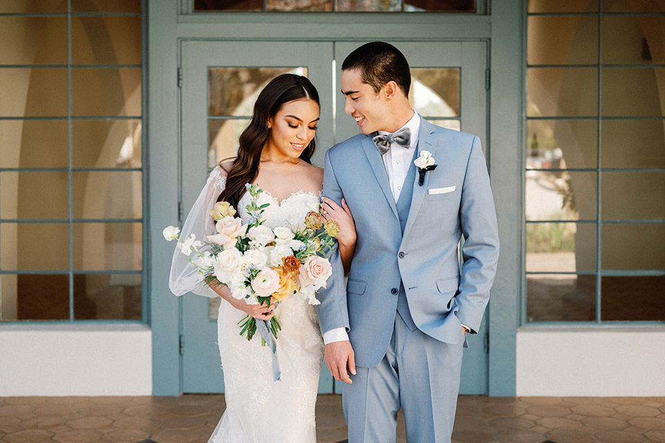  a wedding at the grand gimeno with white, blue, and gold accents – the bride wore a long sleeved modern fitted gown and the groom wore a light blue suit with velvet bow tie – couple at the ceremony