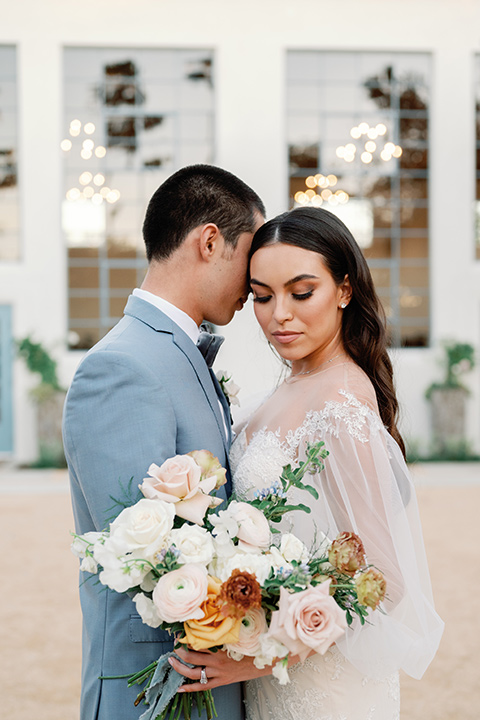 a wedding at the grand gimeno with white, blue, and gold accents – the bride wore a long sleeved modern fitted gown and the groom wore a light blue suit with velvet bow tie – couple sitting by fireplace