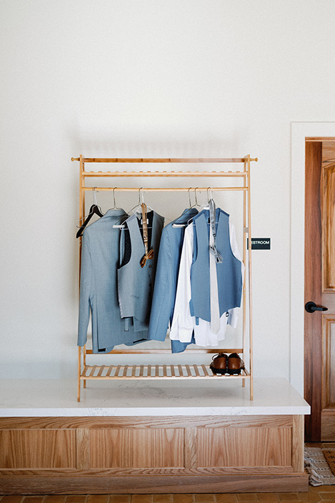 a wedding at the grand gimeno with white, blue, and gold accents – the bride wore a long sleeved modern fitted gown and the groom wore a light blue suit with velvet bow tie – grooms outfit on a coat rack 
